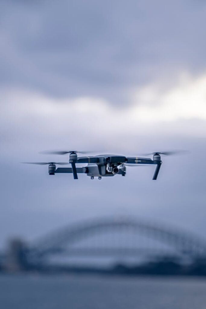 A drone hovers in front of the iconic Sydney Harbor Bridge against a cloudy sky.